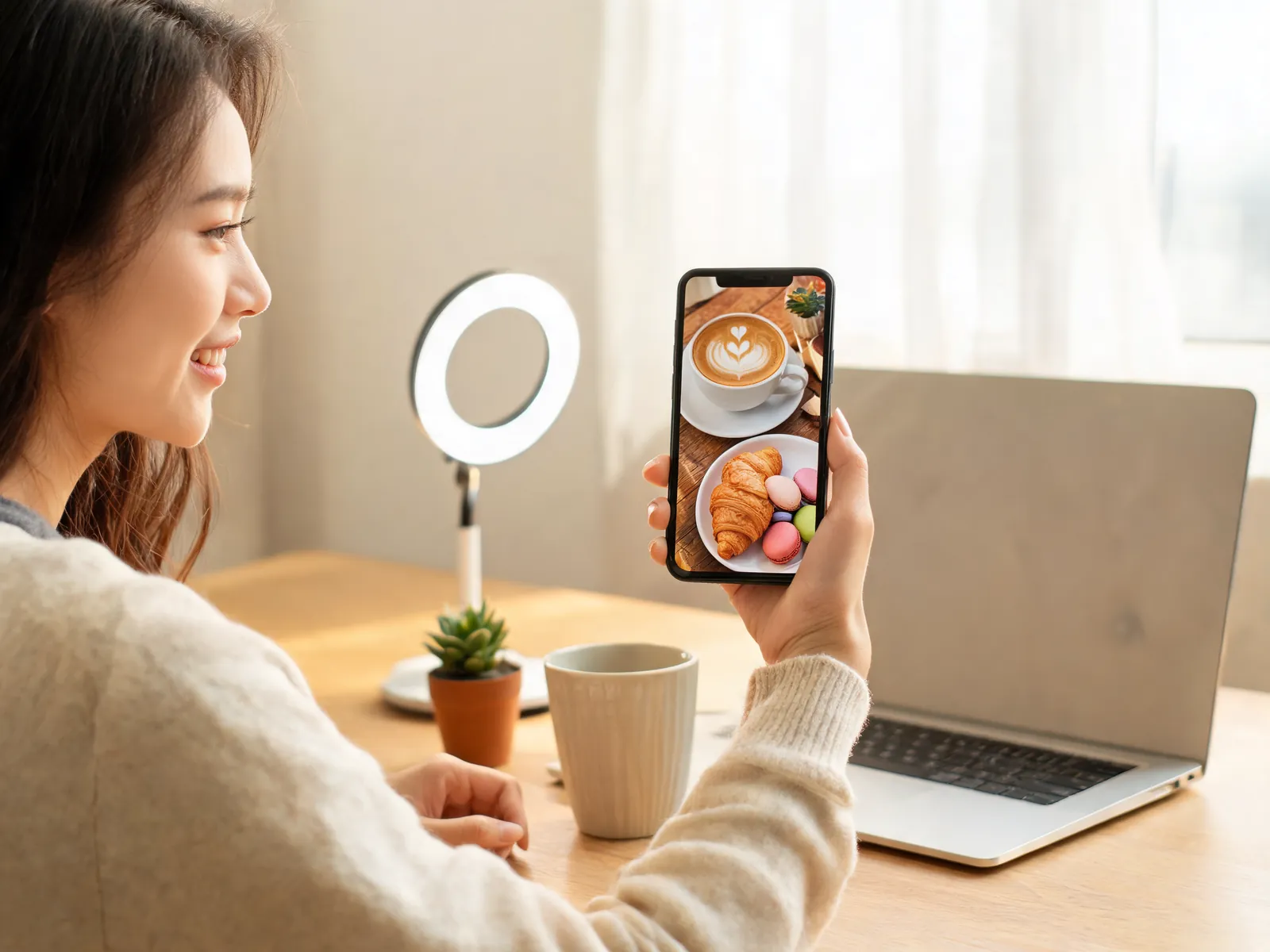 A content creator at a home desk looking at a latte-and-pastries photo on her phone, ready to post to social media.
