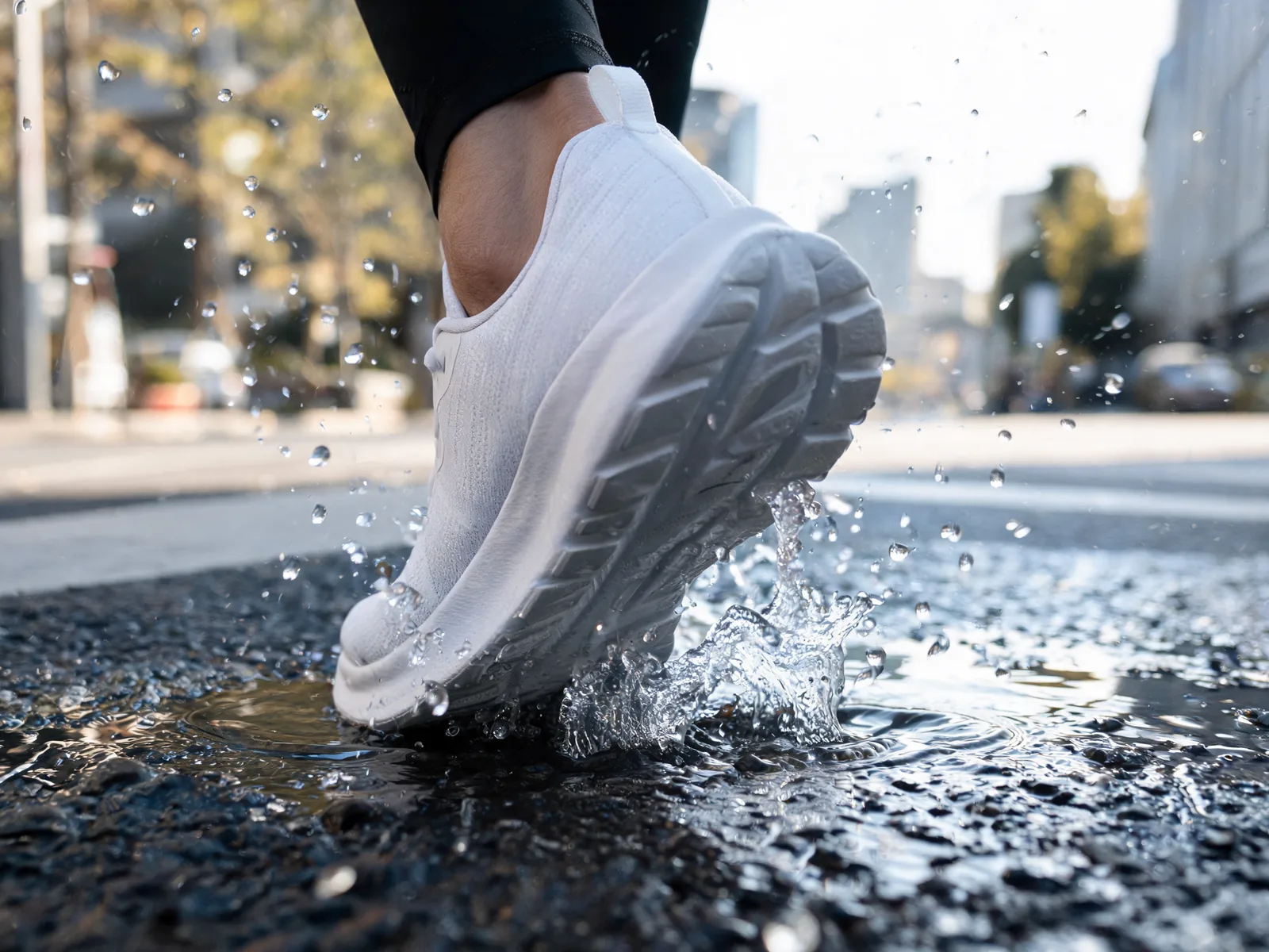 A video ad concept frame: a white running shoe splashing through a puddle on a sunny city street.